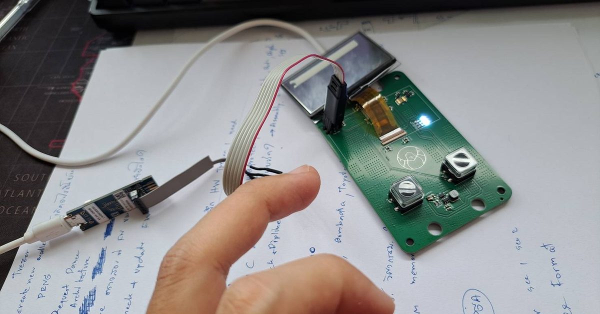 The PHYLAX board on the bench with its OLED panel and SWD programmer attached, on top of handwritten design notes