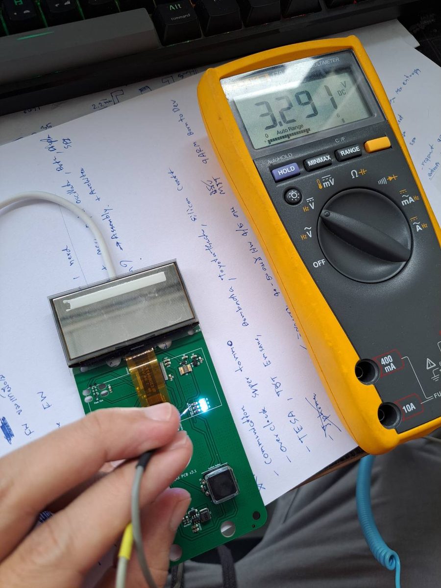 A multimeter reading 3.291 volts DC probed on the PHYLAX board next to the OLED panel